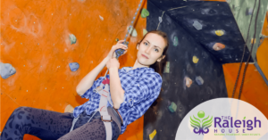 Young woman scales an indoor rock climbing wall during treatment for painkiller addiction.