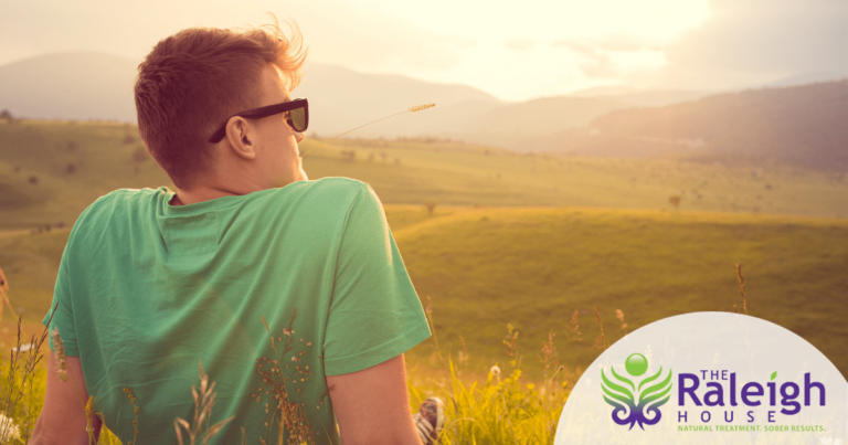 A man with a piece of straw in his mouth looking out at rolling hills.