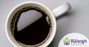 A cup of coffee on a saucer scattered with coffee beans.