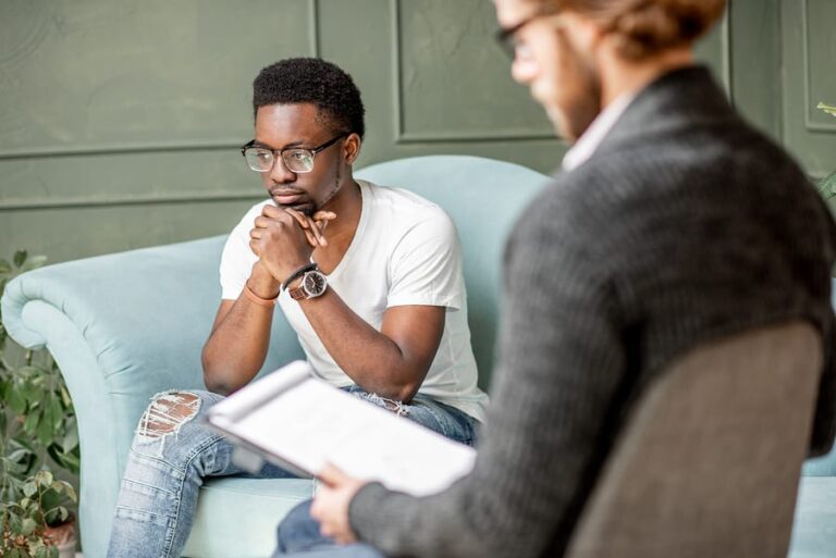 A young man sitting on a couch talking about his mental health with a therapist.