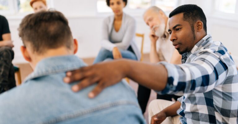 back view of unrecognizable sad man sharing life problem grief with multiracial people in modern mental health support group session in rehab center.