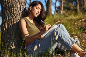 Young woman journaling outside by a tree