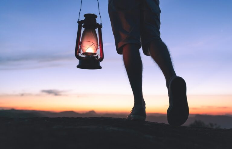 Walking at night while carrying a kerosene lamp to light the way, with sky after sunset in the background.