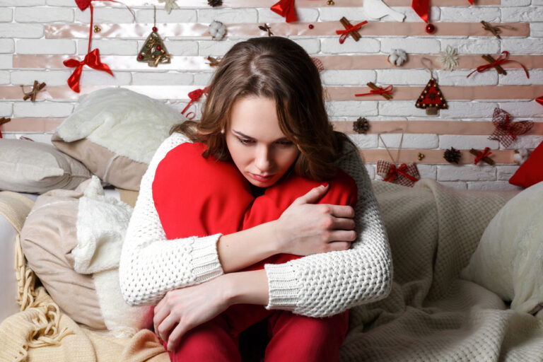 Unhappy young woman sitting alone in bed during the holidays