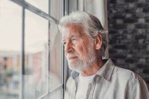 Pensive elderly mature senior man looking in distance out of window, thinking of personal problems.