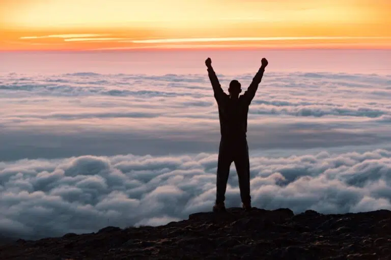 Man with hands stretched up on hike in mountains above the clouds